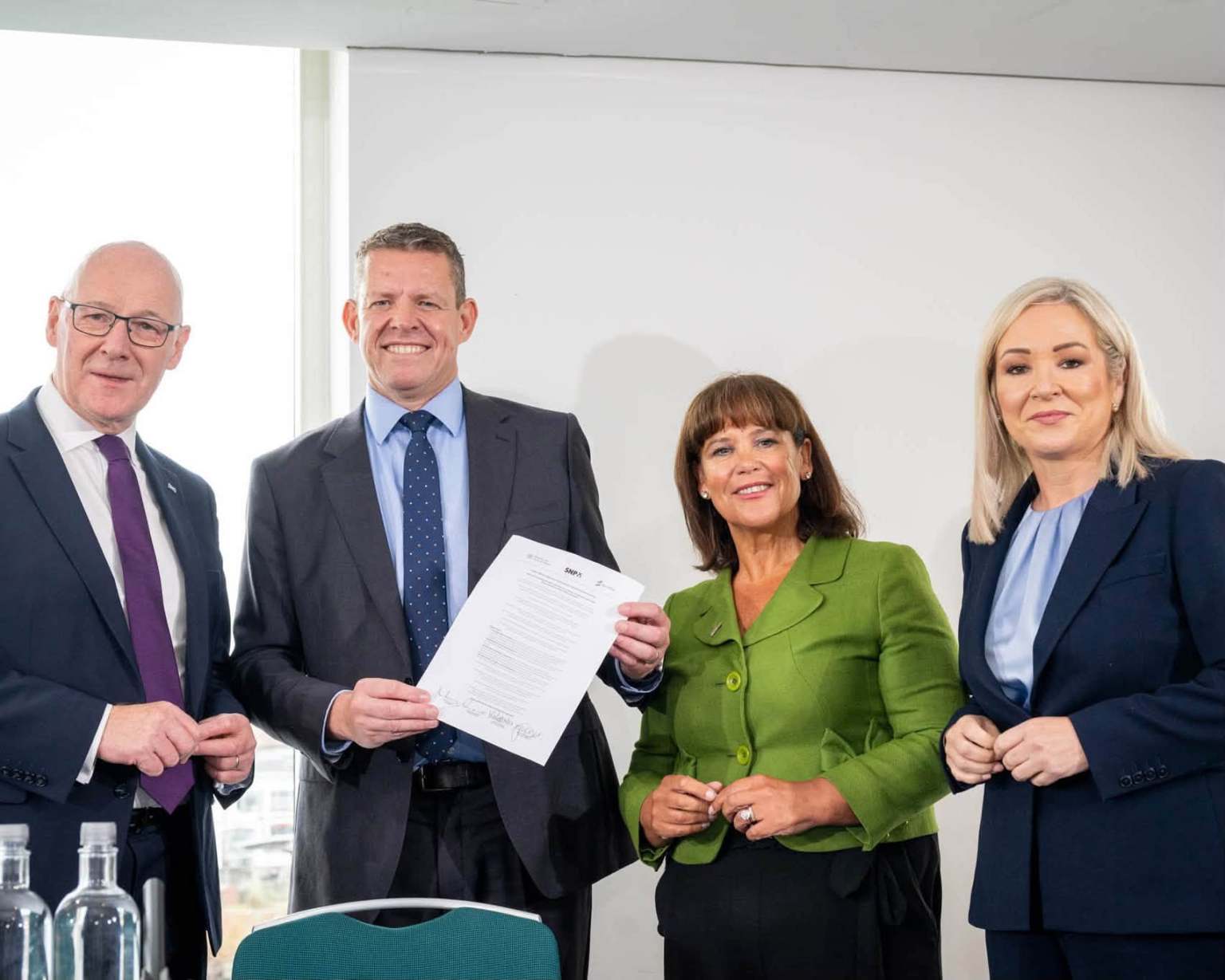 Four party representatives stand together in Cardiff with a copy of the agreement held up.