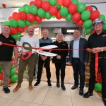 Six people stand beneath a red and green balloon arch with a ribbon and oversized scissors at the SPAR opening.