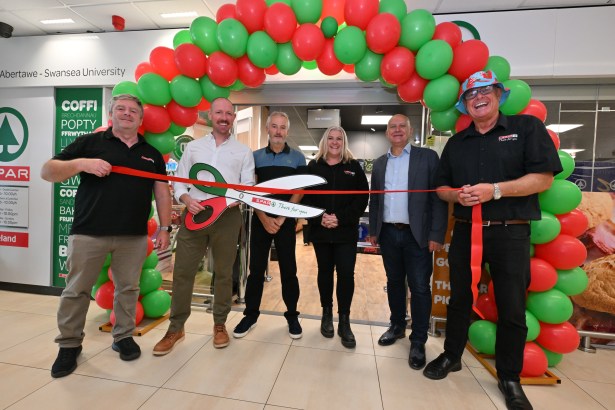 Six people stand beneath a red and green balloon arch with a ribbon and oversized scissors at the SPAR opening.