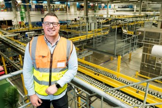 Chris Bailey in a hi-vis vest leaning on a railing above the conveyor lines inside Amazon's Swansea fulfilment centre
