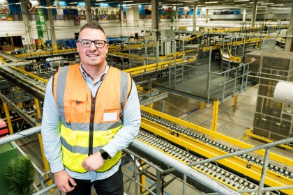 Chris Bailey in a hi-vis vest leaning on a railing above the conveyor lines inside Amazon's Swansea fulfilment centre