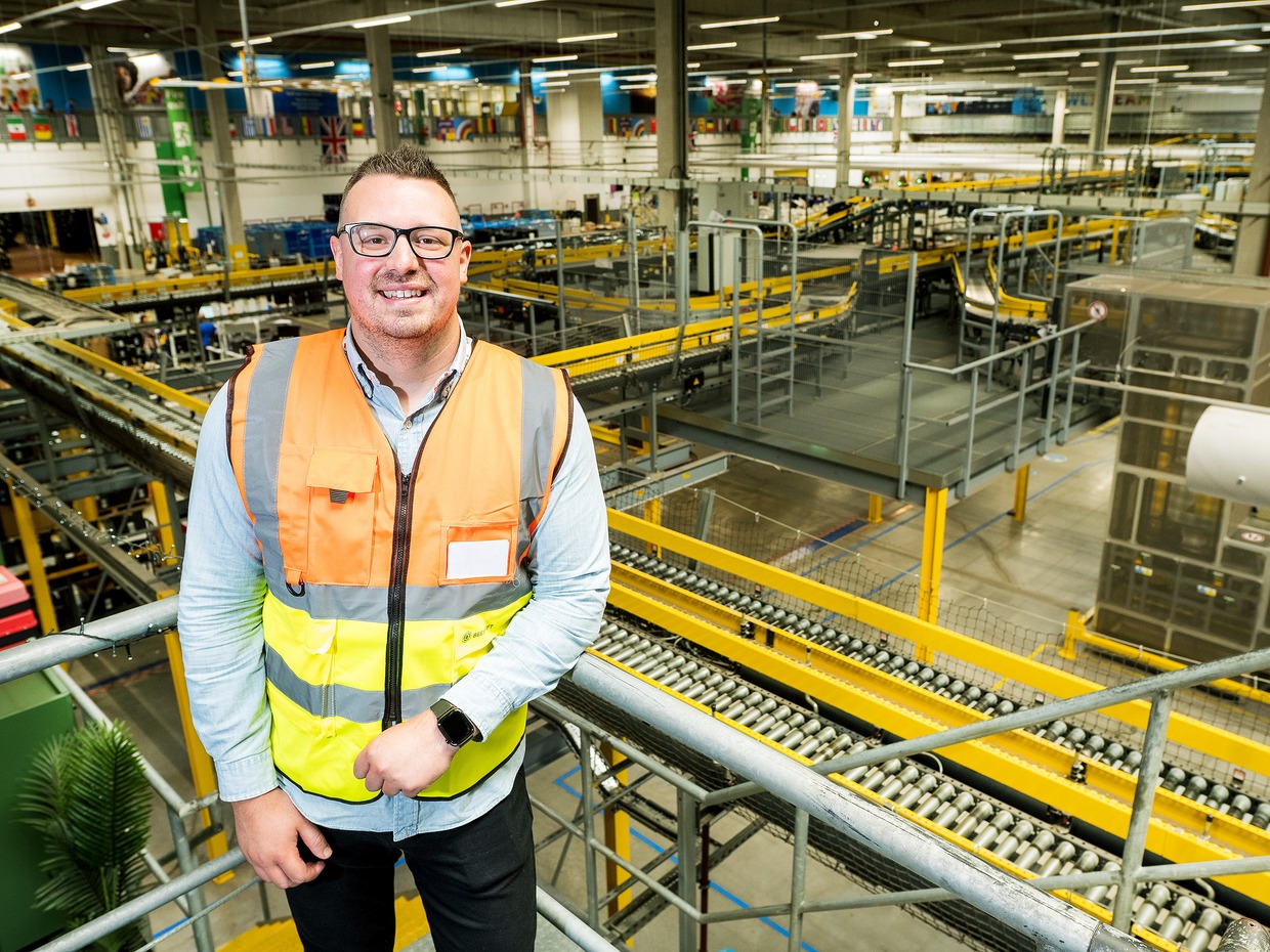 Chris Bailey in a hi-vis vest leaning on a railing above the conveyor lines inside Amazon's Swansea fulfilment centre