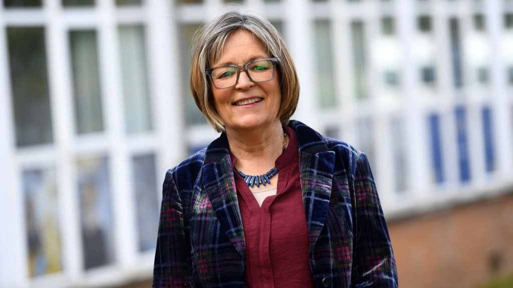 Cabinet Minister for Education and the Welsh Language Anna Brychan smiling in a plaid velvet jacket outside a school building