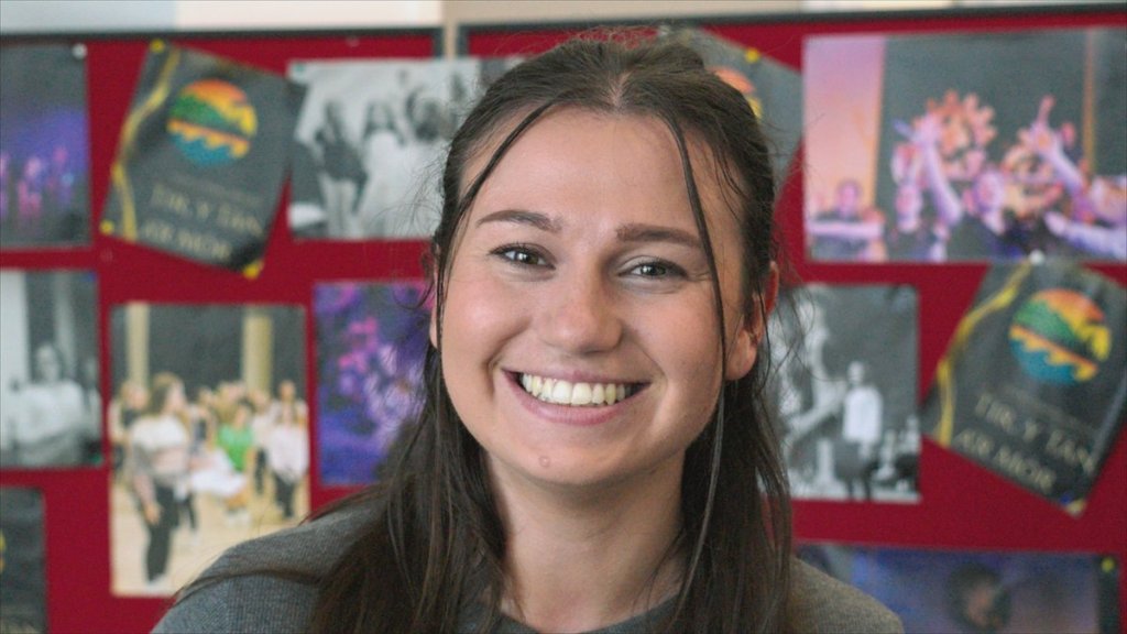 Lowri Whitrow, Welsh teacher at Ysgol Gymraeg Ystalyfera Bro Dur, smiling in front of a display of school show posters in the S4C series Athrawon
