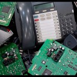 A pile of decommissioned office desk phones and green circuit boards awaiting recycling