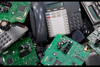 A pile of decommissioned office desk phones and green circuit boards awaiting recycling