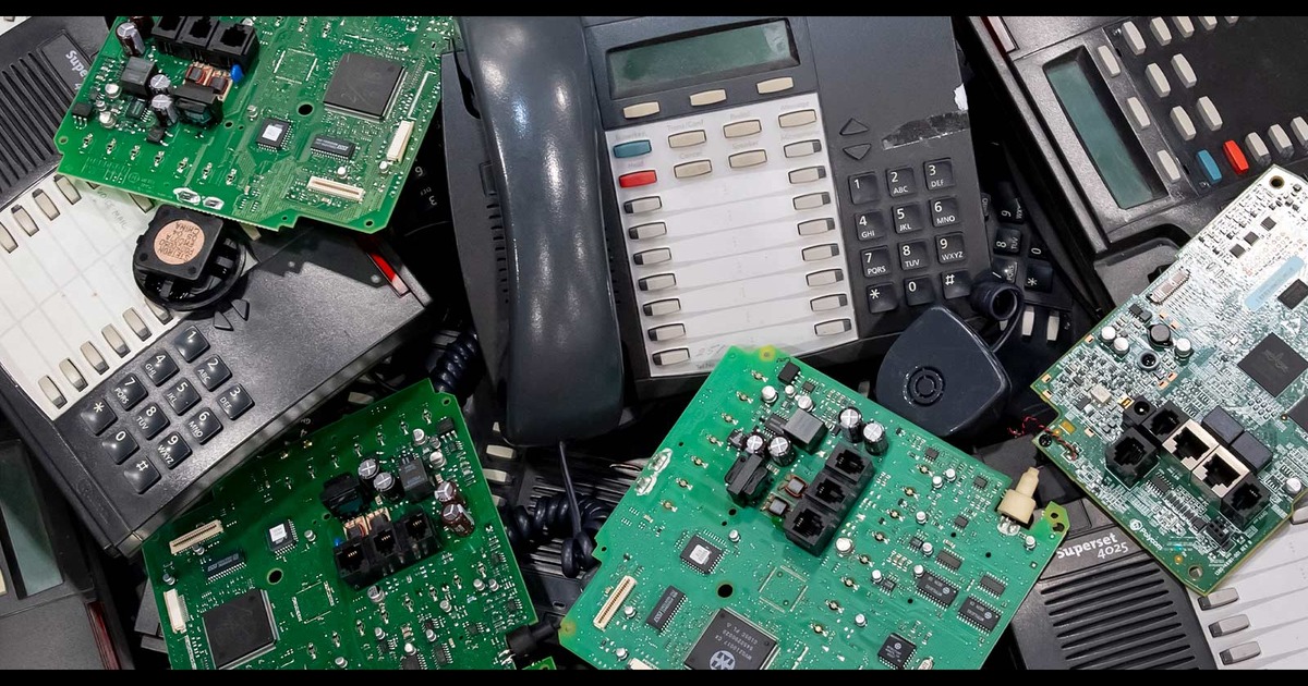 A pile of decommissioned office desk phones and green circuit boards awaiting recycling