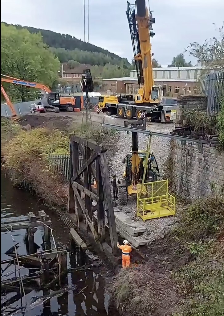 A timber trestle standing in the River Tawe beside the Bascule Bridge with a worker in orange hi-vis alongside it