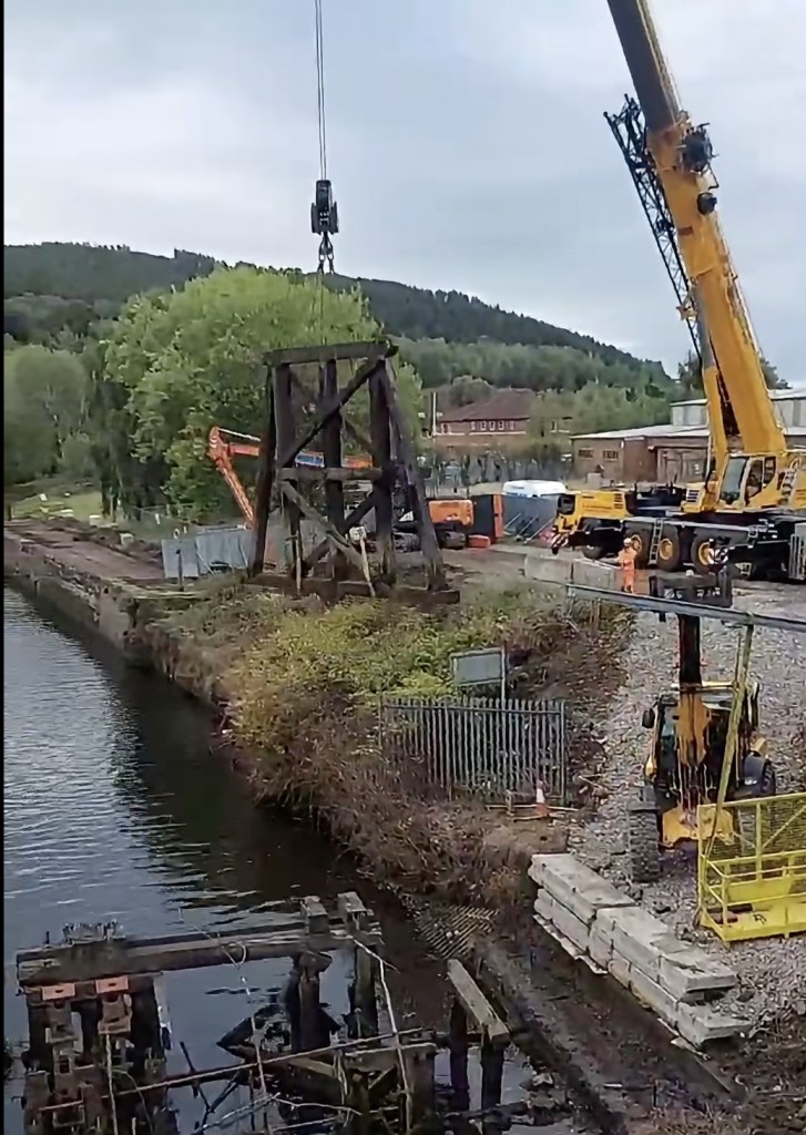 An old timber trestle suspended from a crane hook above the River Tawe