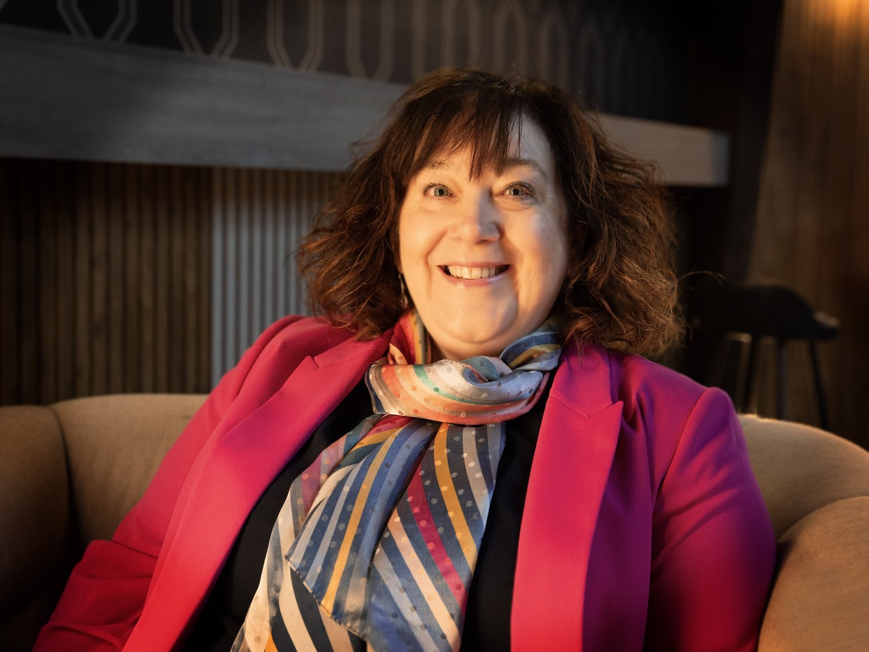 Bethan Evans smiling, seated in an armchair in a pink blazer and striped silk scarf