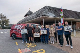 A group of campaigners holding "Jobs not rubble" and "Stop the demolition" placards beside a red Buzz Trampoline Park van outside the former Wilko store in Carmarthen