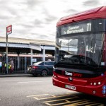 A red TrawsCymru T1 bus signed Lampeter for Aberystwyth pulling away from the kerb outside Carmarthen railway station, with the platform canopy and taxi rank behind