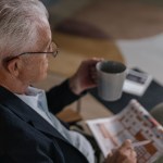 An older man at home with a mug of tea and a puzzle book