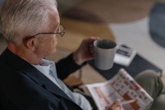 An older man at home with a mug of tea and a puzzle book