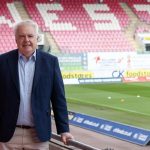 Former First Minister Carwyn Jones in a navy blazer pitchside at Parc y Scarlets, with rows of red seats behind him