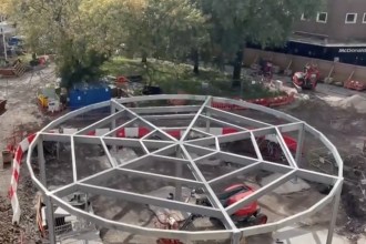 Circular steel frame of a pavilion under construction on the Castle Square Gardens site, with diggers and trees behind