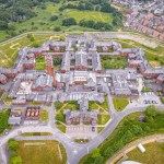 Aerial view of the red-brick Cefn Coed Hospital in Swansea, a symmetrical complex of wards around a central water tower, with housing to one side and fields beyond