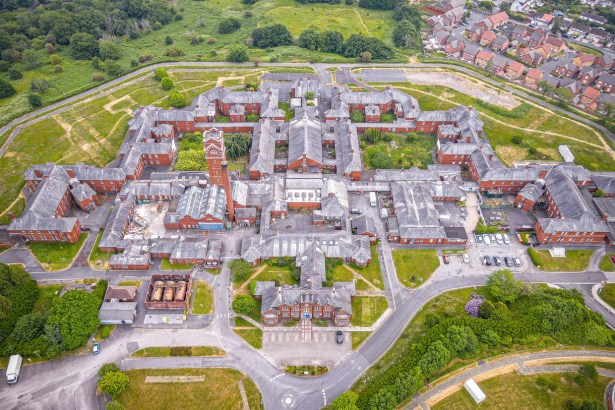 Aerial view of the red-brick Cefn Coed Hospital in Swansea, a symmetrical complex of wards around a central water tower, with housing to one side and fields beyond