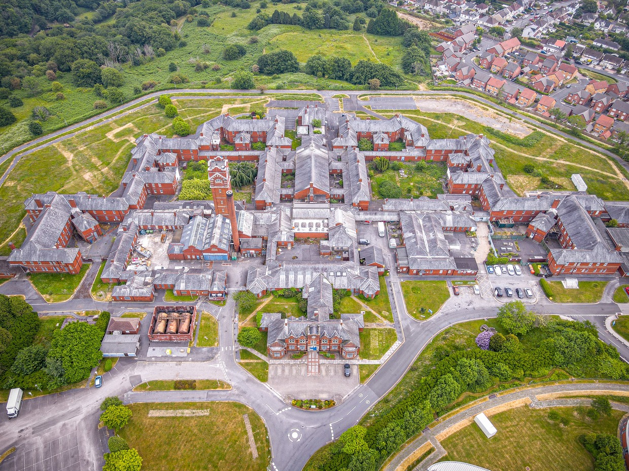 Aerial view of the red-brick Cefn Coed Hospital in Swansea, a symmetrical complex of wards around a central water tower, with housing to one side and fields beyond