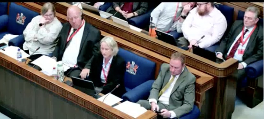 Cllr Andrea Harrington seated at a laptop in the council chamber with council leader Rob Stewart beside her