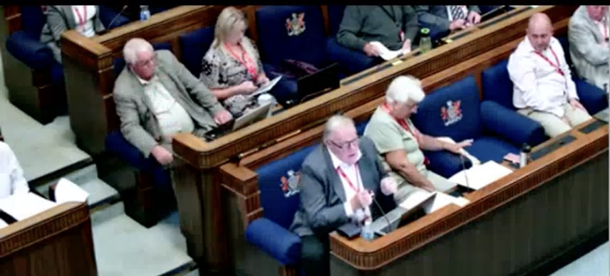Cllr Chris Holley speaking into a microphone from his seat in the council chamber