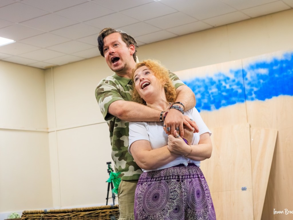 Stefan Pejic hugging a fellow cast member from behind during rehearsals, both laughing