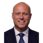 Official Senedd portrait of Dan Thomas MS, smiling in a navy suit and polka dot tie against a white background