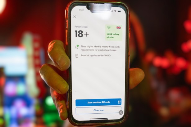 A hand holding a phone in a bar showing a digital proof of age screen reading 18+ and valid to buy alcohol