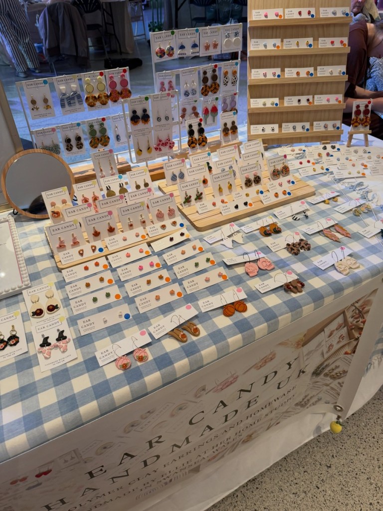 Close-up of dozens of colourful polymer clay earrings on white cards laid out on a blue gingham stall cloth