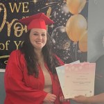 Natalie Price Pettersson in a red graduation cap and gown holding her certificates beside a Faith in Families staff member, in front of a celebration banner