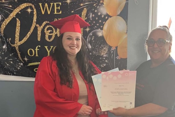 Natalie Price Pettersson in a red graduation cap and gown holding her certificates beside a Faith in Families staff member, in front of a celebration banner