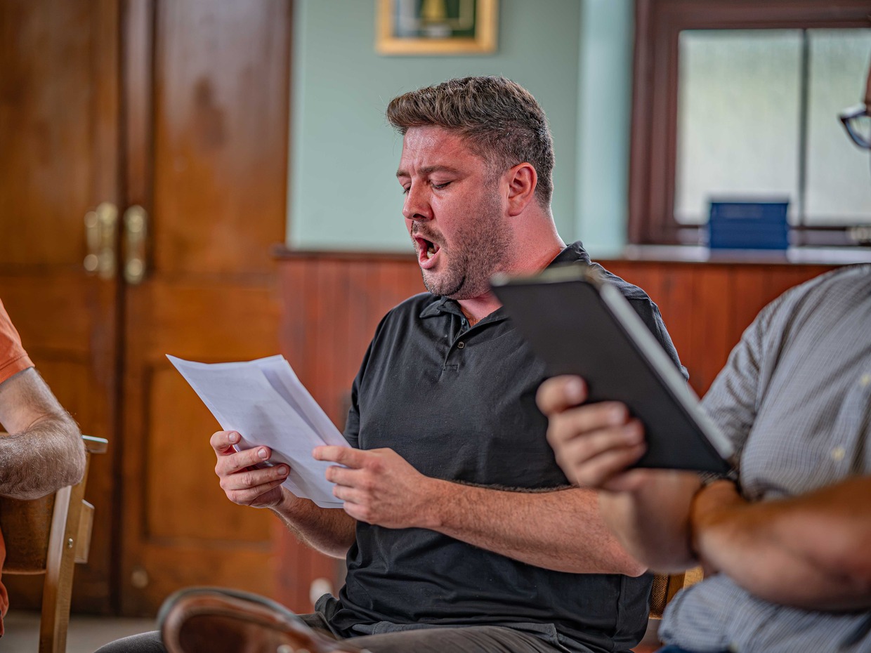 Baritone Emyr Wyn Jones singing from sheet music during a rehearsal for Fflamau Penyberth