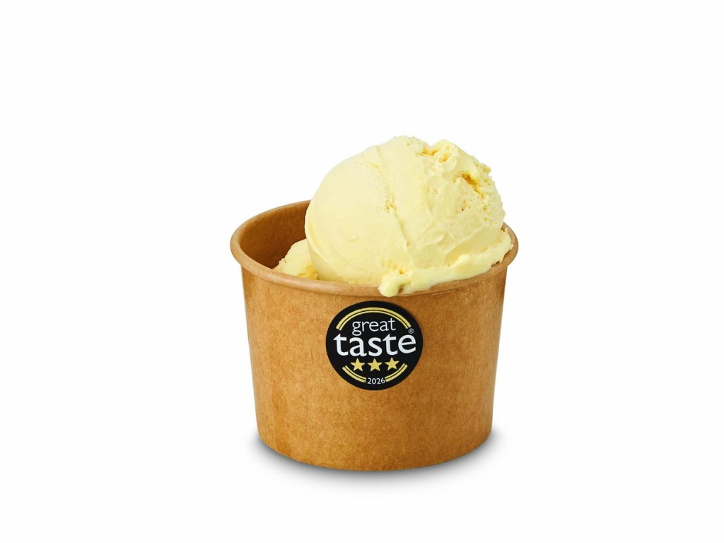 A scoop of pale yellow sorbet in a brown card tub carrying a three-star Great Taste 2026 sticker