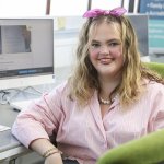Georgia Miggins smiling in a pink striped shirt and pink hair bow at a computer desk in a Swansea Lifelong Learning classroom