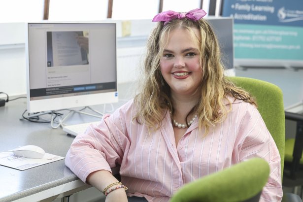 Georgia Miggins smiling in a pink striped shirt and pink hair bow at a computer desk in a Swansea Lifelong Learning classroom