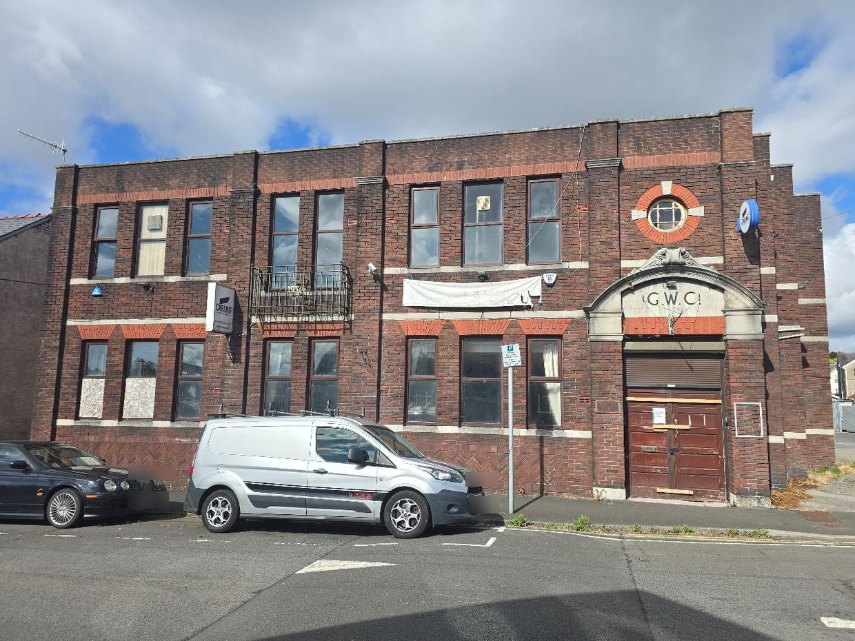 Two-storey red-brick former working men's club on Brighton Road, Gorseinon, with G.W.C. carved above a shuttered doorway and windows boarded