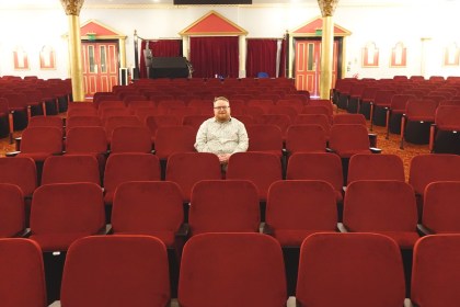 Cllr Elliott King sitting alone among the rows of new red seats in the stalls at Swansea Grand Theatre