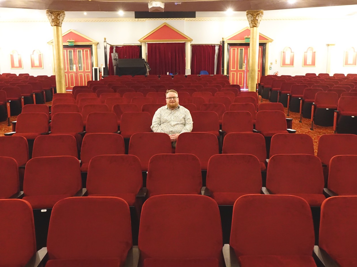Cllr Elliott King sitting alone among the rows of new red seats in the stalls at Swansea Grand Theatre
