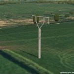 Computer-generated image of a slim grey steel pole with a Y-shaped top carrying power lines across green farmland, with trees and hills behind