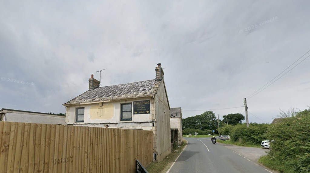 The stripped pub gable seen from the road, with a Kings Head pub sign still fixed to it advertising real fires four miles ahead