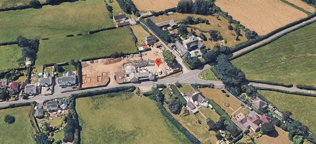 Aerial view of the former Greyhound Inn site showing the stripped pub building beside cleared ground with house foundations marked out