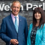 Nigel Farage in a blue suit and Helen Jenner in a turquoise jacket standing in front of the slate wall and Welsh Parliament sign at the Senedd