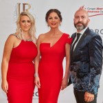 Jess Rice and Catherine Zeta-Jones in red evening dresses and Jamie Rice in a floral velvet jacket, in front of a JR and Swansea Council sponsor board