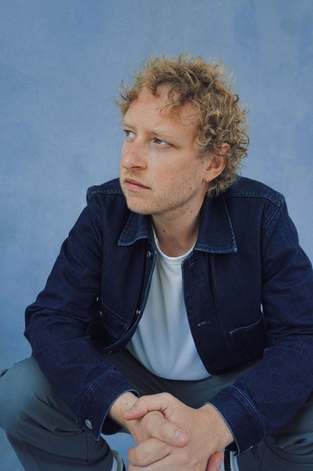 Jazz pianist Joe Webb in a denim jacket crouching against a pale blue background