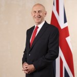 Chancellor John Healey in a dark suit and red tie, smiling in front of a Union flag in his official ministerial portrait