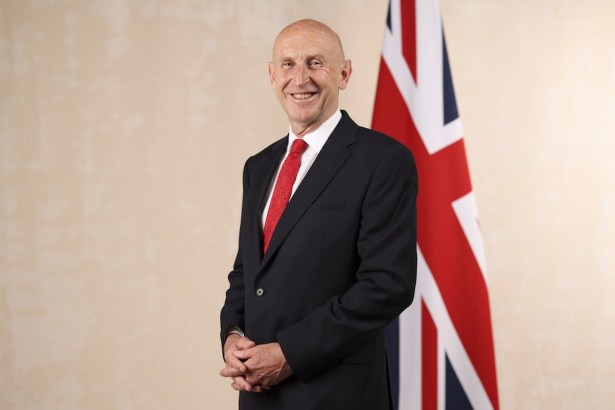 Chancellor John Healey in a dark suit and red tie, smiling in front of a Union flag in his official ministerial portrait