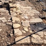 The excavated remains of a stone building on Kilvey Hill's summit, showing a flagged stone floor and low wall stub behind temporary fencing