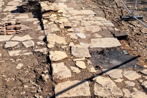 The excavated remains of a stone building on Kilvey Hill's summit, showing a flagged stone floor and low wall stub behind temporary fencing
