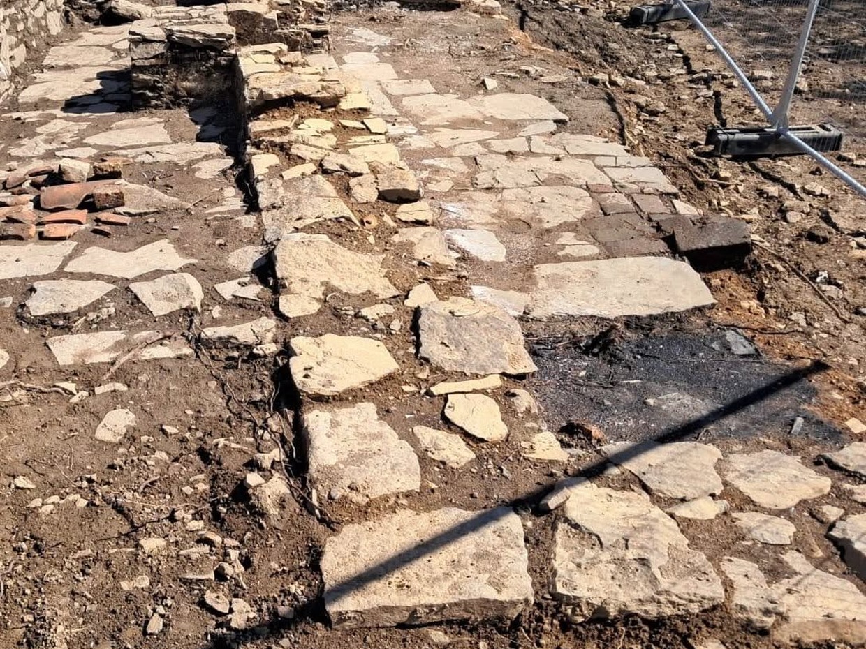 The excavated remains of a stone building on Kilvey Hill's summit, showing a flagged stone floor and low wall stub behind temporary fencing