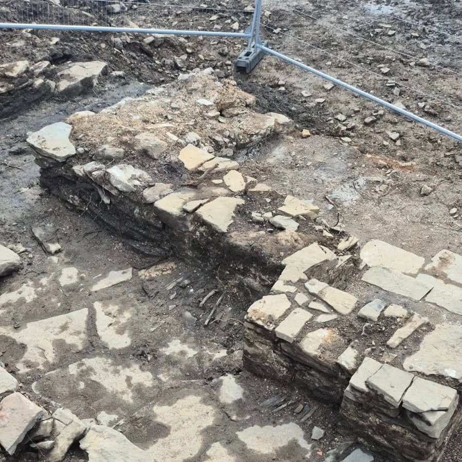 Low courses of stone wall forming the corner of the excavated building on Kilvey Hill, behind temporary fencing